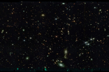 Black space with thousands of stars and tiny swirling galaxies.