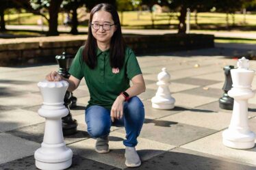 woman kneels down beside oversized queen chess piece