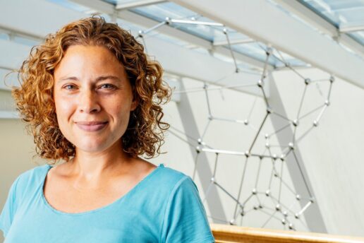 Photo of Danna Freedman indoors with a molecular sculpture hanging from the ceiling behind her
