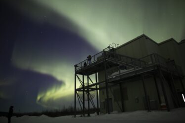 Aurora visible above a building and observation platform with two people silhouetted at night